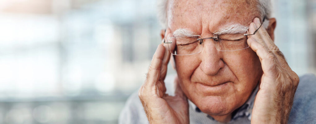 Older man with closed eyes touching both sides of his head in pain