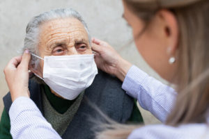 A woman puts a surgical mask on the face of an elderly patient