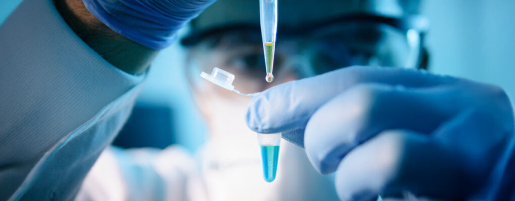 A lab technical uses a dropper to add liquid to a test vial